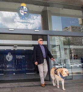 Alberto Calcagno, fundador de FUNDAPPAS, sale de la Torre Ejecutiva de la Presidencia de la República, en Montevideo, acompañado por su perro guía. En la imagen, Calcagno camina junto al perro, sujeto por su arnés de guía, frente a la entrada del edificio de Presidencia Uruguay.