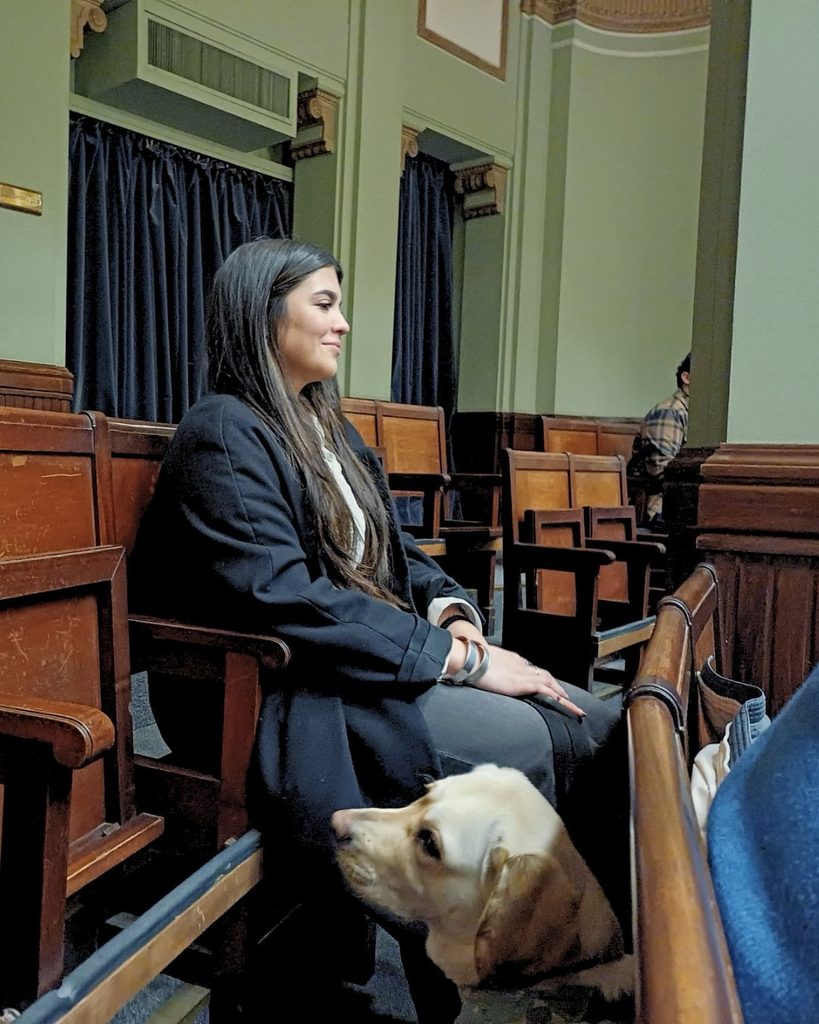 Socializadora sentada junto a un perro de asistencia en formación durante una instancia parlamentaria vinculada a la creación del Día Nacional del Socializador de Perros de Asistencia.